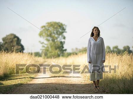 Woman standing on edge of dirt road, next to field View Large Photo Image Stock Photo - Woman standing on edge of dirt road, next to field. Fotosearch