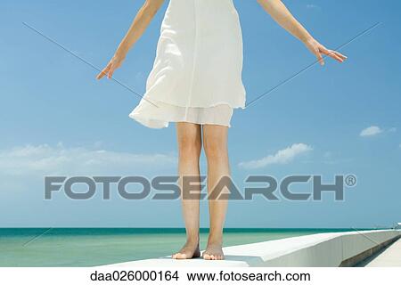 Woman standing on low wall at the beach, arms out, low angle view, cropped View Large Photo Image Picture - Woman standing on low wall at the beach, arms out, low angle view, cropped. Fotosearch