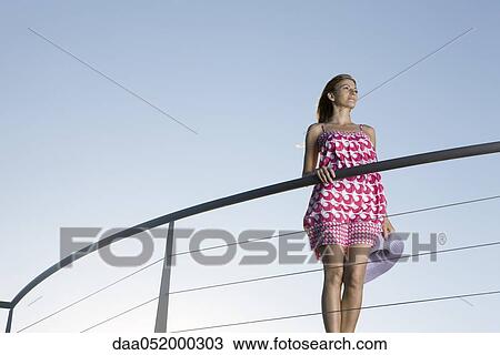 Stock Image - Woman standing on outdoor balcony, looking away in thought. Fotosearch