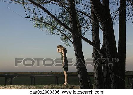 Stock Photograph - Woman standing on tiptoes outdoors, holding head and looking down. Fotosearch