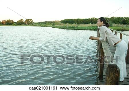 Woman standing on wooden footbridge over lake, looking into distance View Large Photo Image Stock Image - Woman standing on wooden footbridge over lake, looking into distance. Fotosearch