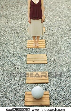 Stock Image - Woman standing opposite sphere on footpath in gravel, high angle view, cropped. Fotosearch