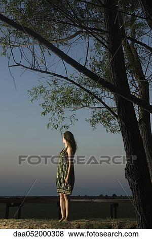 Stock Photo - Woman standing outdoors at twilight, looking over shoulder at view. Fotosearch