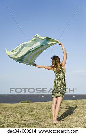 Woman standing outdoors, holding up shawl in wind, full length View Large Photo Image Picture - Woman standing outdoors, holding up shawl in wind, full length. Fotosearch