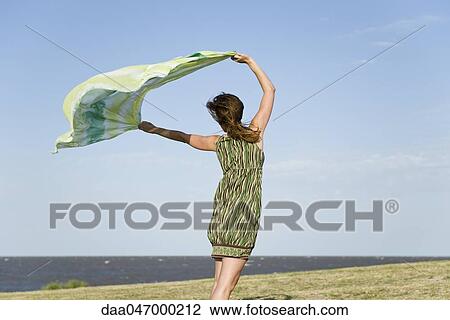 Woman standing outdoors, holding up shawl in wind, full length View Large Photo Image Stock Image - Woman standing outdoors, holding up shawl in wind, full length. Fotosearch