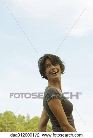 Woman standing outdoors, smiling over shoulder View Large Photo Image Stock Image - Woman standing outdoors, smiling over shoulder. Fotosearch