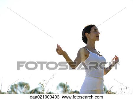 Stock Image - Woman standing outdoors with arms in yoga pose, low angle view. Fotosearch
