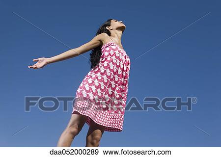 Woman standing outdoors with arms out and eyes closed, low angle view View Large Photo Image Stock Photo - Woman standing outdoors with arms out and eyes closed, low angle view. Fotosearch