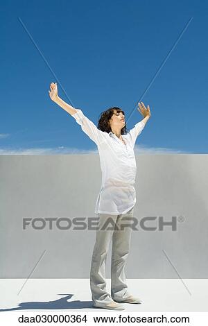 Woman standing outdoors with arms raised, eyes closed View Large Photo Image Picture - Woman standing outdoors with arms raised, eyes closed. Fotosearch