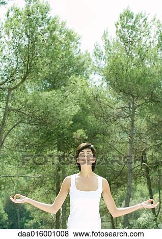 Stock Photo - Woman standing with arms out, eyes closed, trees in background. Fotosearch