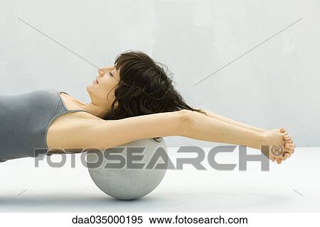 Stock Photography - Woman stretching using fitness ball placed at base of head, arms raised. Fotosearch