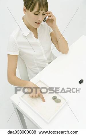 Woman talking on cell phone, drawing in rock garden with finger View Large Photo Image Stock Photo - Woman talking on cell phone, drawing in rock garden with finger. Fotosearch