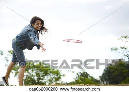 Stock Image - Woman throwing flying disc at park. Fotosearch