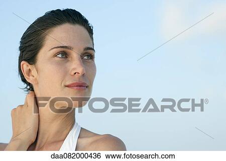 Stock Photograph - Woman touching neck, looking up in thought. Fotosearch