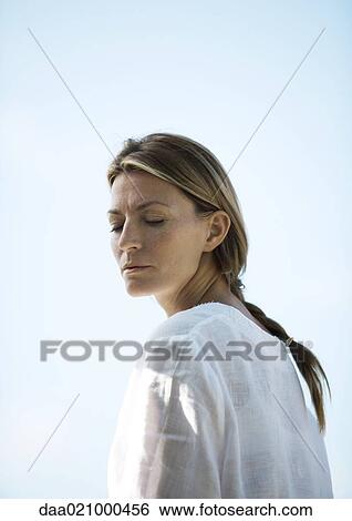 Woman turning head, eyes half-closed, low angle view View Large Photo Image Stock Photograph - Woman turning head, eyes half-closed, low angle view. Fotosearch
