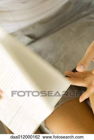 Stock Image - Woman turning pages of book, partial view. Fotosearch