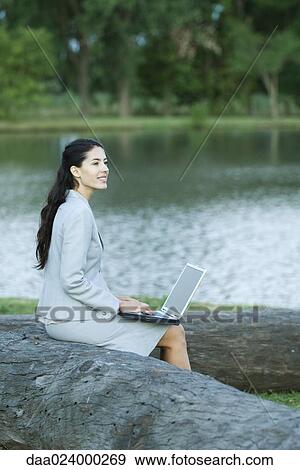 Woman using laptop in park, lake in background View Large Photo Image Stock Photo - Woman using laptop in park, lake in background. Fotosearch