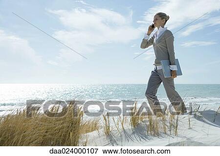 Woman walking across dunes, using cell phone, carrying laptop under arm View Large Photo Image Stock Photo - Woman walking across dunes, using cell phone, carrying laptop under arm. Fotosearch