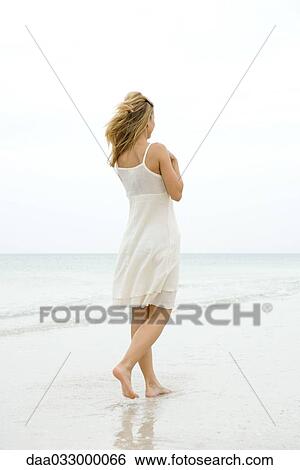 Stock Photograph - Woman walking at the beach in the surf, rear view. Fotosearch
