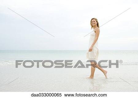 Woman walking at the beach in the surf, smiling at camera View Large Photo Image Stock Photography - Woman walking at the beach in the surf, smiling at camera. Fotosearch