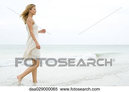 Stock Photography - Woman walking at the beach, side view. Fotosearch