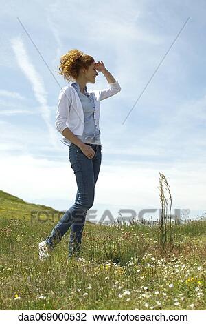 Woman walking in meadow, shading eyes with hand View Large Photo Image Stock Image - Woman walking in meadow, shading eyes with hand. Fotosearch