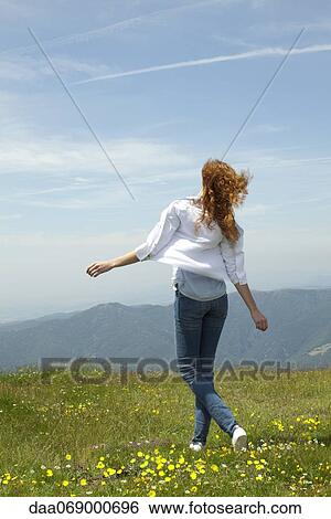 Stock Photograph - Woman walking through meadow with arms outstretched. Fotosearch