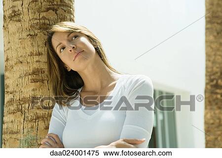 Stock Photography - Woman with arms crossed, leaning against palm tree. Fotosearch