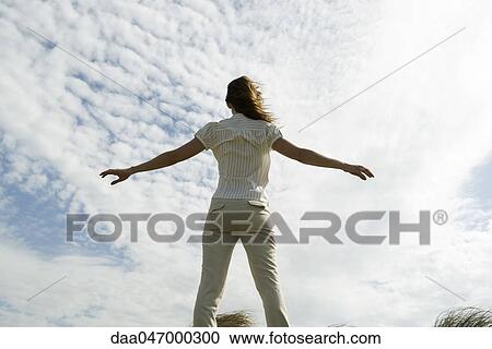 Woman with arms outstretched, cloudy sky in background, rear view View Large Photo Image Stock Image - Woman with arms outstretched, cloudy sky in background, rear view. Fotosearch