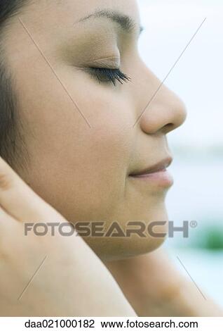 Stock Image - Woman with hands against side of face, eyes closed, profile, extreme close-up. Fotosearch