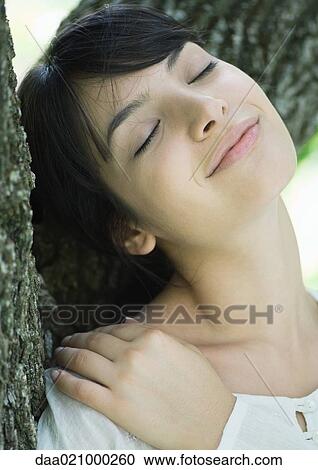 Woman with head against tree trunk, eyes closed, smiling View Large Photo Image Stock Image - Woman with head against tree trunk, eyes closed, smiling. Fotosearch