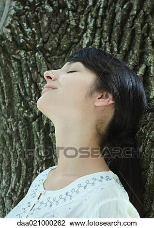 Woman with head against tree trunk, eyes closed, smiling View Large Photo Image Stock Image - Woman with head against tree trunk, eyes closed, smiling. Fotosearch