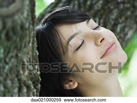 Woman with head against tree trunk, eyes closed, smiling View Large Photo Image Stock Photo - Woman with head against tree trunk, eyes closed, smiling. Fotosearch