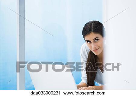 Stock Image - Woman with laptop, smiling at camera, cropped view. Fotosearch