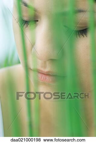 Stock Photo - Woman's face, eyes closed, vegetation in foreground. Fotosearch