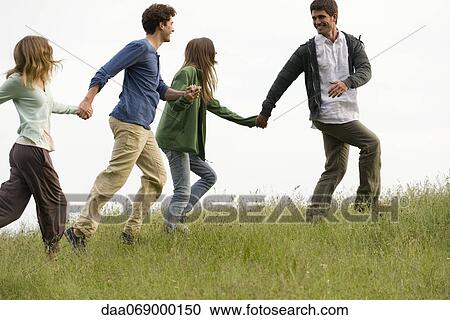 Stock Image - Young adults running on meadow holding hands. Fotosearch