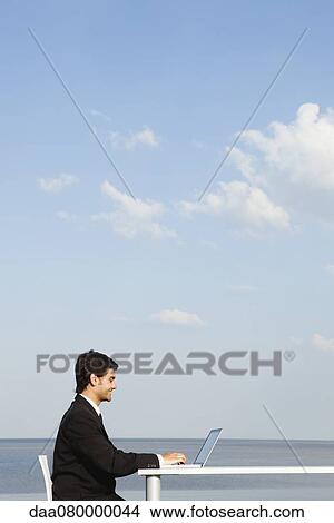 Young businessman working at desk by ocean, side view View Large Photo Image Picture - Young businessman working at desk by ocean, side view. Fotosearch