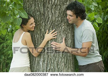 Young couple leaning against tree trunk, smiling at each other View Large Photo Image Stock Photo - Young couple leaning against tree trunk, smiling at each other. Fotosearch