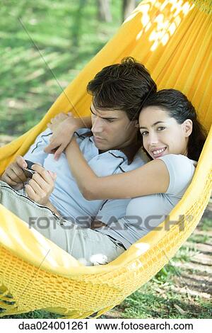 Young couple lying in hammock, using digital camera, woman smiling at camera View Large Photo Image Stock Image - Young couple lying in hammock, using digital camera, woman smiling at camera. Fotosearch