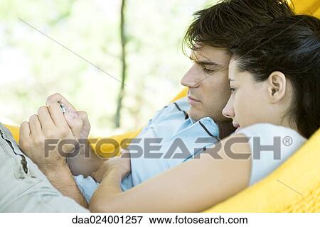 Young couple lying in hammock, using digital camera View Large Photo Image Stock Photo - Young couple lying in hammock, using digital camera. Fotosearch
