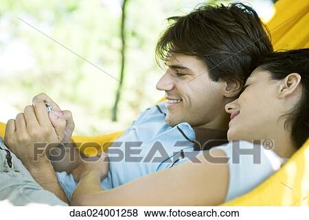 Young couple lying in hammock, using digital camera View Large Photo Image Stock Photo - Young couple lying in hammock, using digital camera. Fotosearch