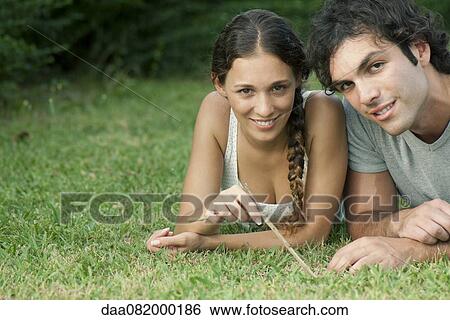 Stock Photograph - Young couple lying together on grass, portrait. Fotosearch