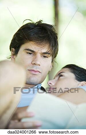 Stock Photograph - Young couple, man reading while woman looks at him, head on his shoulder. Fotosearch