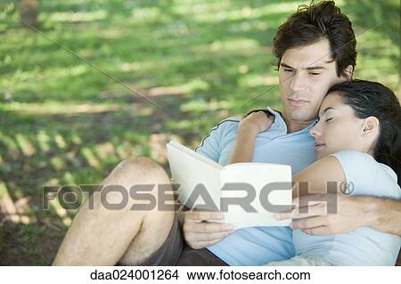 Young couple outdoors, man reading while woman sleeps with head on his shoulder View Large Photo Image Picture - Young couple outdoors, man reading while woman sleeps with head on his shoulder. Fotosearch