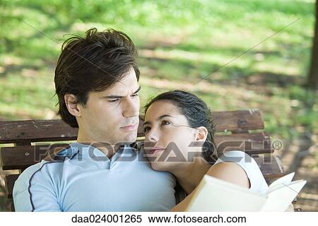 Young couple outdoors, man reading while woman looks at him, head on his shoulder View Large Photo Image Stock Photography - Young couple outdoors, man reading while woman looks at him, head on his shoulder. Fotosearch