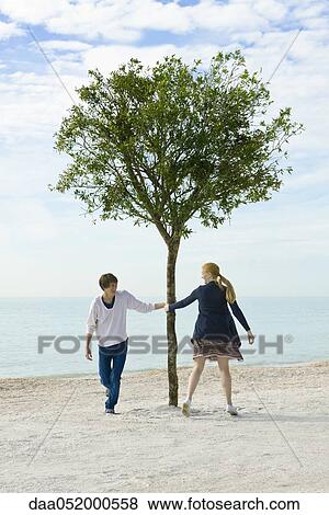Stock Photo - Young couple playfully pursuing one another around tree. Fotosearch