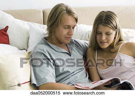 Stock Photography - Young couple reading magazine together in bed. Fotosearch