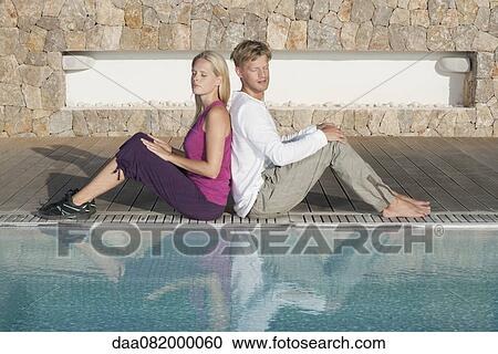 Young couple sitting back to back at poolside View Large Photo Image Stock Image - Young couple sitting back to back at poolside. Fotosearch