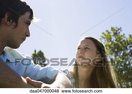 Stock Photo - Young couple sitting outdoors, looking at each other. Fotosearch
