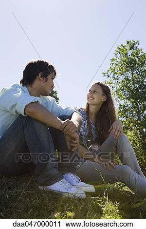 Stock Image - Young couple sitting together on grass. Fotosearch